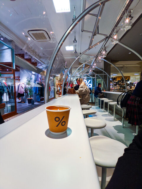 Interior of % Arabica café in Kyoto Kawaramachi with its sleek minimalist design, long white counter seating, and signature coffee cup with the % logo.
