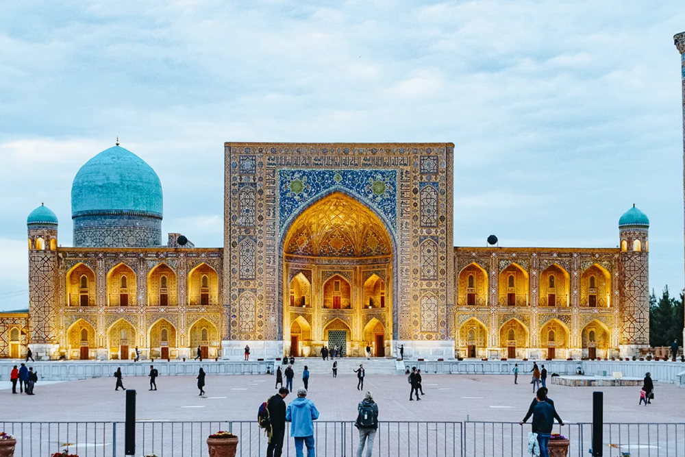 Illuminated Registan Square with grand madrasa facade and blue dome at dusk in Samarkand