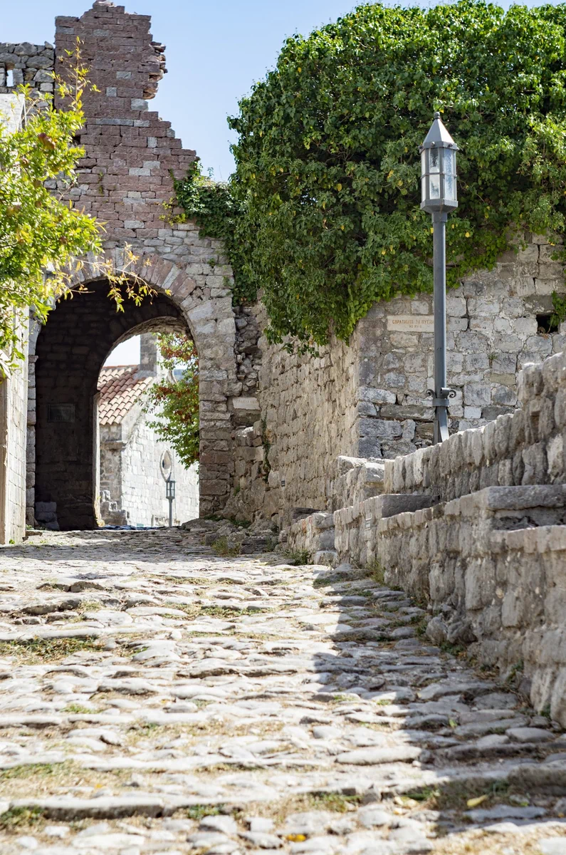 Empty cobblestone street in Stari Bar with a stone arch, vintage lamp post and overgrown walls, Montenegro