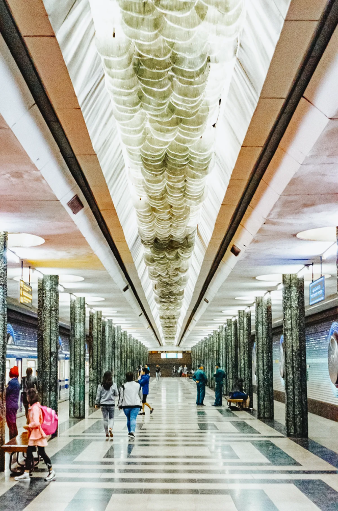 Interior of Kosmonavtlar metro station in Tashkent with columns, chandelier ceiling and passengers